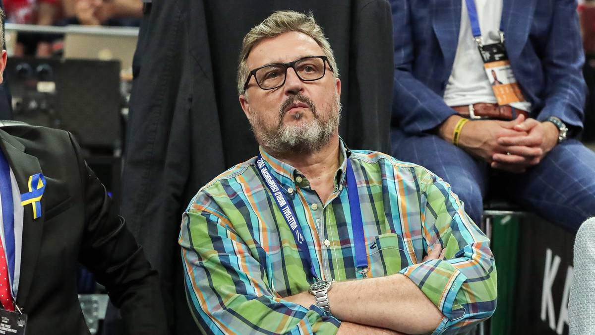 Portret mężczyzny w okularach i koszuli w kratkę z rękami założonymi na piersi.