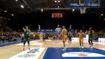 Mecz koszyk&oacute;wki z udziałem zawodnik&oacute;w w zielonych i ż&oacute;łtych strojach na parkiecie hali sportowej.