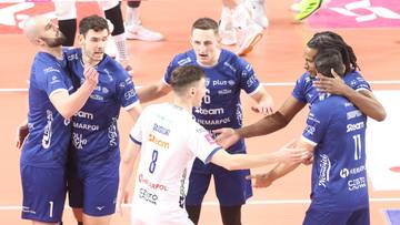 Siatkarze w granatowych strojach otaczają zawodnika w białej koszulce na boisku.