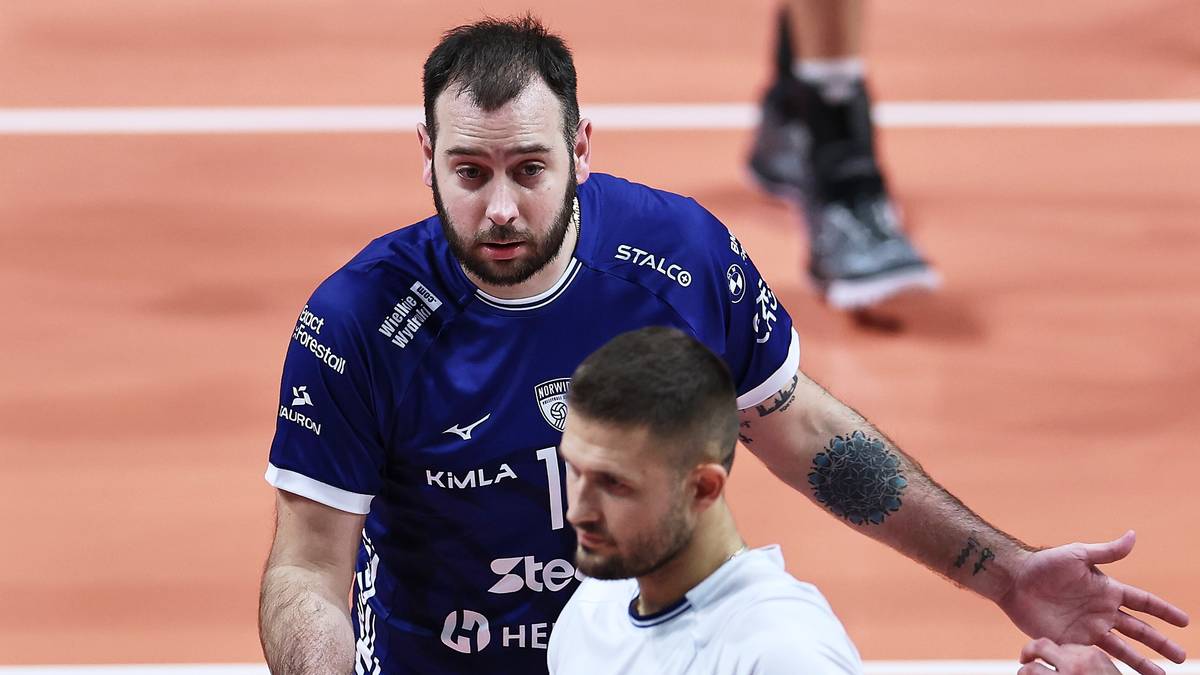 Siatkarze w niebieskich i białych strojach stoją na boisku, jeden z nich rozmawia z drugim.