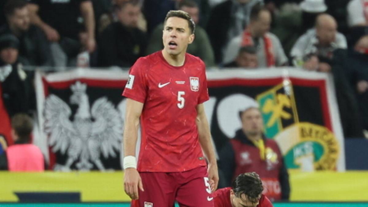 Piłkarz reprezentacji Polski w czerwonej koszulce stoi na boisku z opuszczoną głową.