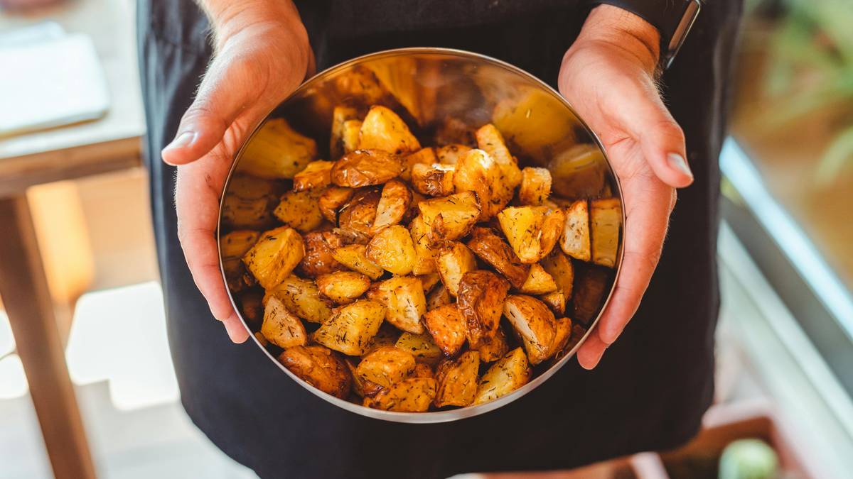 Dłonie trzymające metalową miskę z pokrojonymi i upieczonymi ziemniakami.