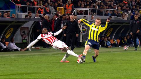 Dw&oacute;ch piłkarzy na boisku piłkarskim podczas meczu, jeden w białej koszulce z czerwonymi pasami pada na ziemię, drugi w ż&oacute;łto-czarnej koszulce prowadzi piłkę.