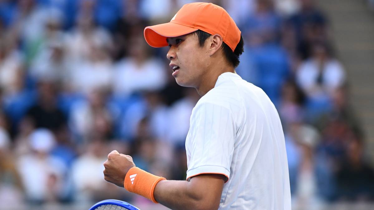 Tenisista w pomarańczowej czapce i białej koszulce zaciśniętą pięścią.