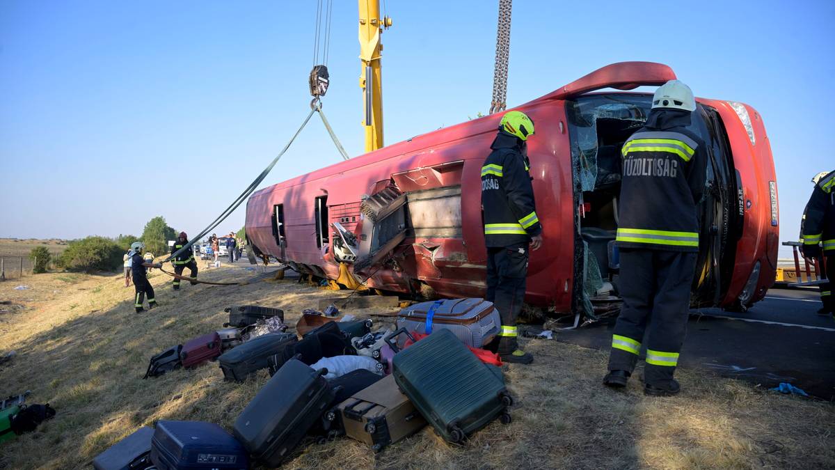 Autobus wypadł z drogi i leży przewr&oacute;cony na boku, a strażacy pr&oacute;bują go podnieść za pomocą dźwigu. Wok&oacute;ł rozrzucony jest bagaż.