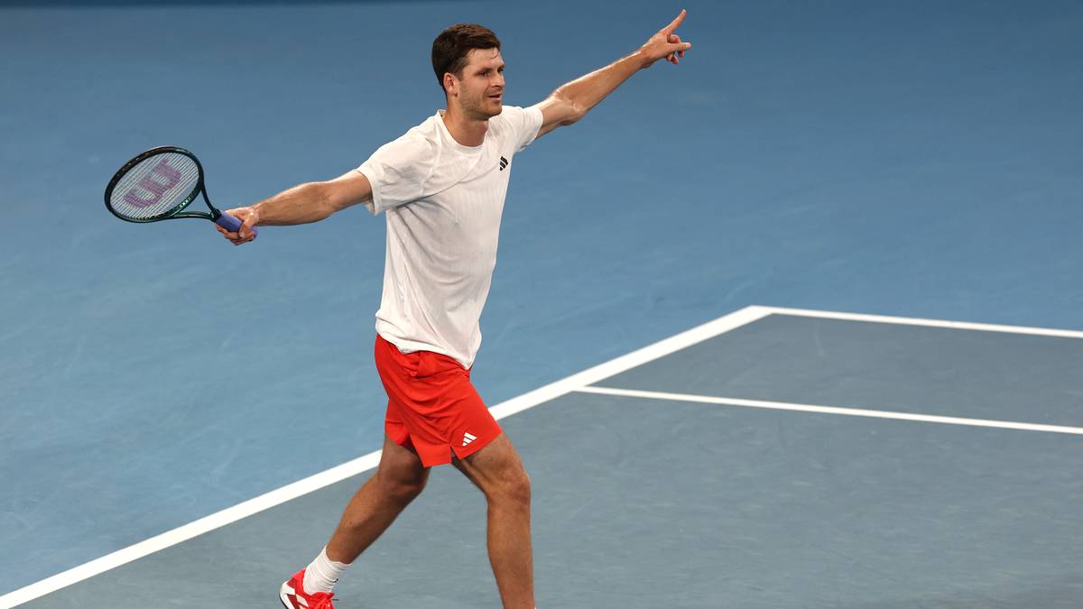 Tenisista w białej koszulce i czerwonych spodenkach świętuje na korcie tenisowym.