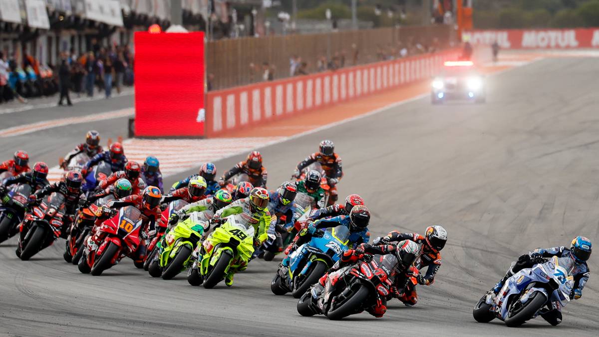 Wyścig motocyklowy z peletonem zawodników na torze, widoczne trybuny i baner "MOTUL"