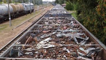 Widok z g&oacute;ry na otwarty wagon kolejowy wypełniony nielegalnymi odpadami, w tle inne wagony towarowe i tory.