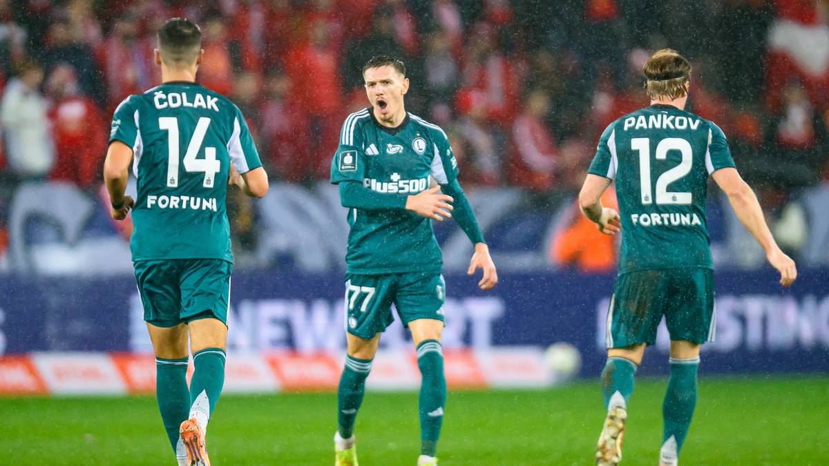 Trzech piłkarzy w zielonych strojach na boisku piłkarskim.