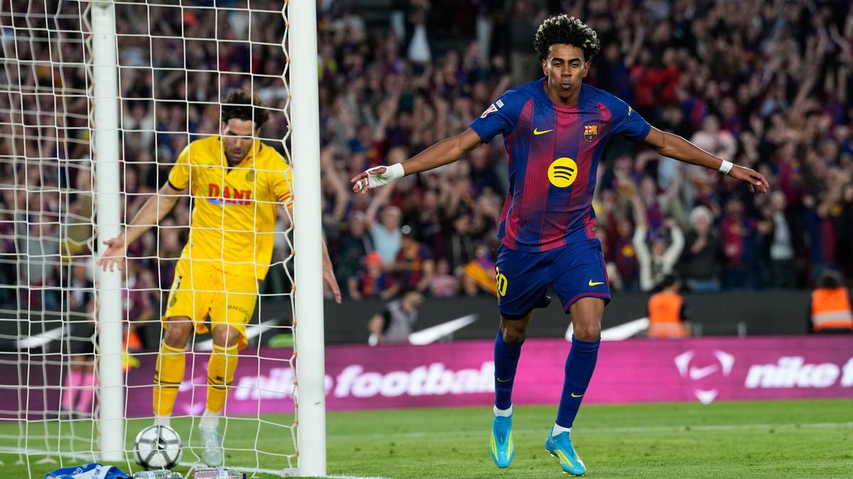 Piłkarz Barcelony w biegu w kierunku bramki, obok niego piłkarz przeciwnika przy siatce bramki.