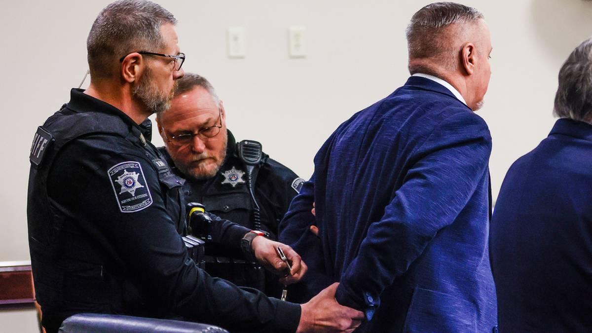 Dw&oacute;ch funkcjonariuszy policji zakłada kajdanki mężczyźnie ubranemu w garnitur.