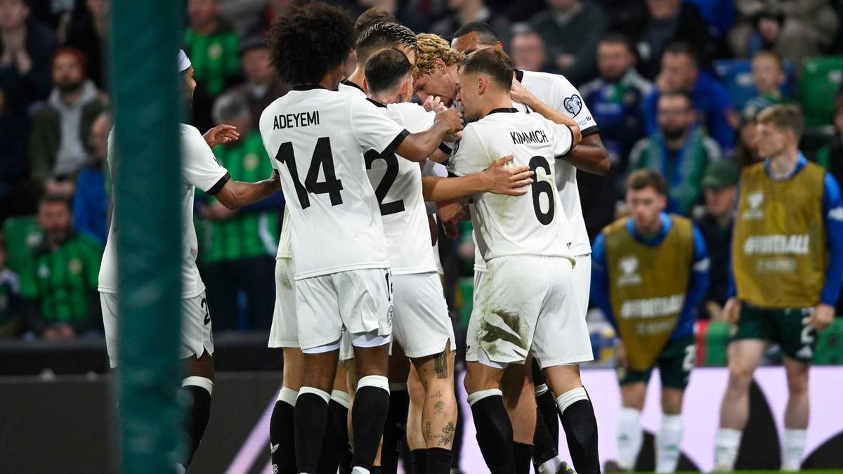 Piłkarze w białych strojach przytulają się świętując bramkę. Na plecach widoczne numery 14 i 6.