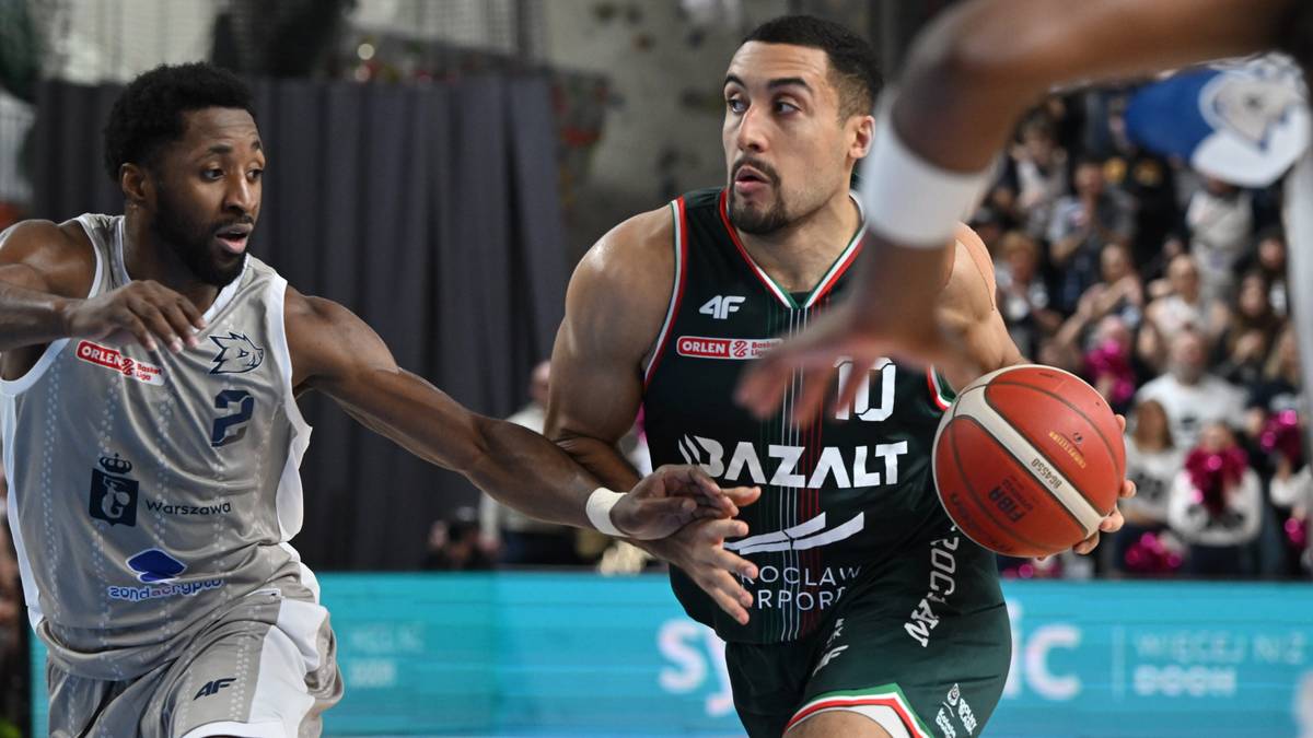 Dw&oacute;ch koszykarzy w akcji podczas meczu. Jeden z zawodnik&oacute;w w zielonym stroju z numerem 10 pr&oacute;buje przejąć piłkę, podczas gdy drugi zawodnik w szarym stroju z numerem 2 usiłuje go powstrzymać.