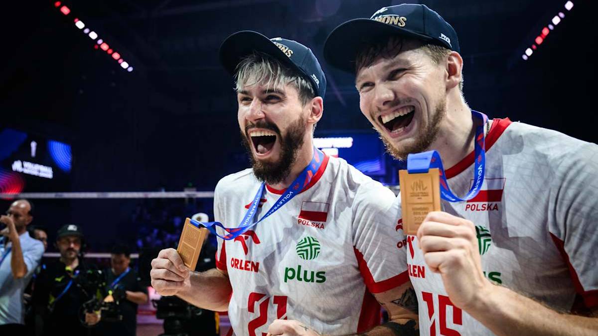 Dwóch siatkarzy w strojach reprezentacji Polski, trzymających medale i cieszących się ze zwycięstwa.