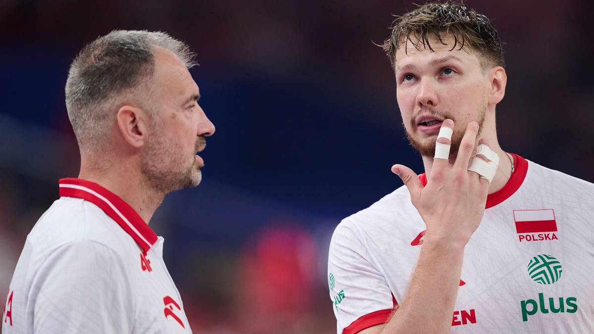 Dwóch polskich siatkarzy w białych strojach reprezentacji Polski rozmawia ze sobą podczas meczu.