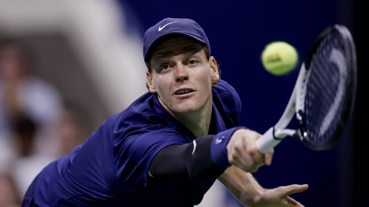 Tenisista w granatowej czapce i stroju podczas uderzenia piłki rakietą podczas meczu.