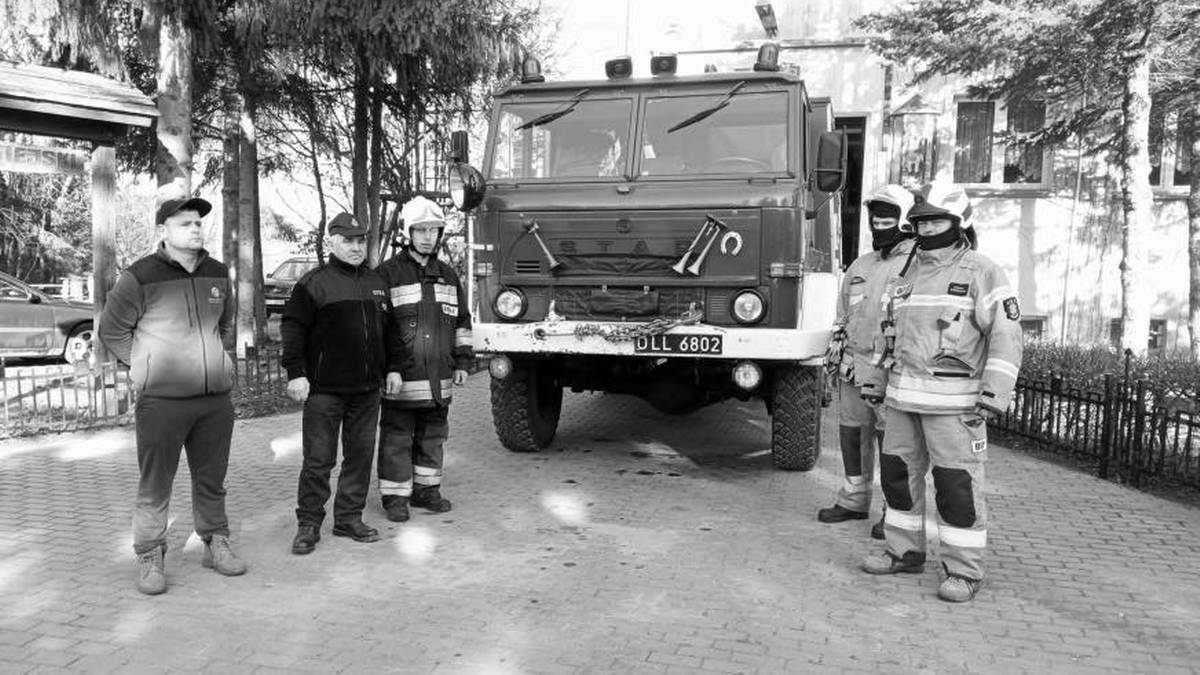 Strażacy stoją przed wozem strażackim.