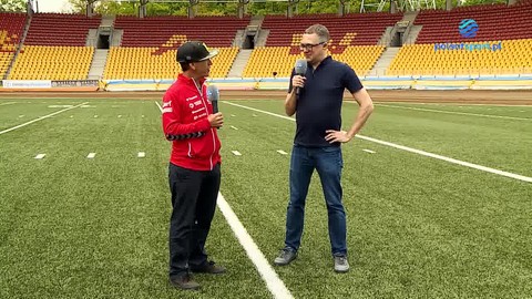 Wywiad z Gregiem Hancockiem na stadionie żużlowym. Dwóch mężczyzn stoi na boisku, jeden z nich jest przeprowadzającym wywiad.