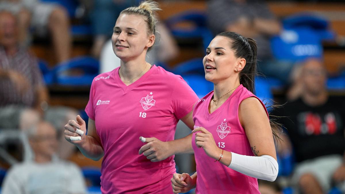 Dwie siatkarki w różowych strojach sportowych biegnące obok siebie na boisku.