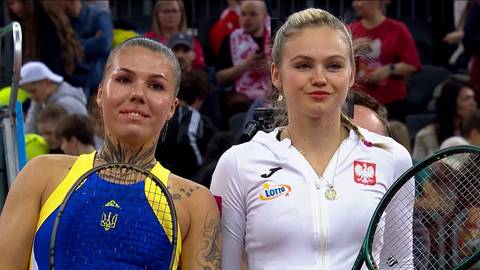 Zdjęcie przedstawia dwie tenisistki: Ołeksandrę Olijnykową (po lewej) i Lindę Klimovicovą (po prawej). Ołeksandra ma na sobie ż&oacute;łto-niebieski str&oacute;j sportowy z logo Ukrainy, a Linda białą bluzę z godłem Polski i logo Lotto. Obie trzymają rakiety tenisowe.