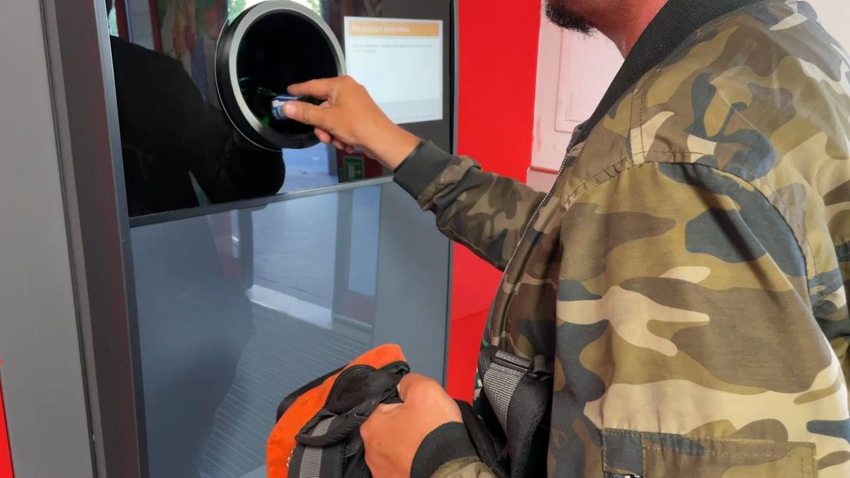 Ręka wrzuca plastikową butelkę do otworu butelkomatu.