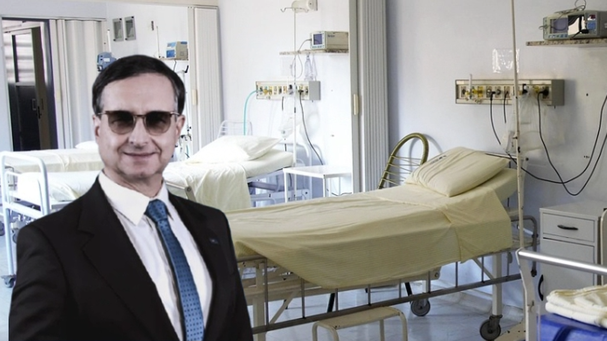 Marek Magierowski w garniturze i okularach przeciwsłonecznych stoi przed łóżkami szpitalnymi.