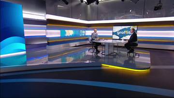 Dwóch mężczyzn w garniturach siedzi naprzeciwko siebie przy okrągłym stole w nowoczesnym studiu telewizyjnym. Na ekranie za nimi widnieje napis "graffiti".