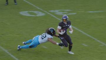 Gracz w czarnym stroju z piłką w rękach biegnie po boisku, podczas gdy gracz w białym stroju próbuje go zatrzymać.