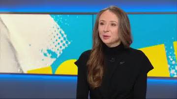 Kobieta w czarnym golfie siedzi przed ekranem z grafikami w niebieskich i ż&oacute;łtych kolorach.