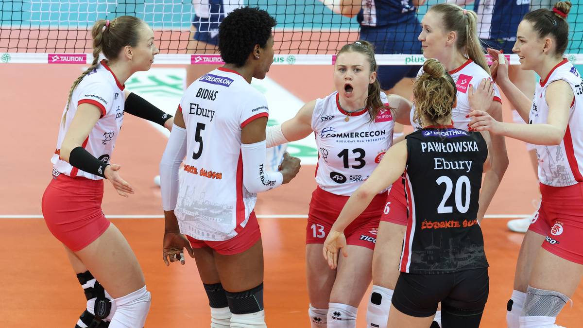 Siatkarki w białych i czarnych strojach sportowych na boisku, jedna z nich krzyczy, inne rozmawiają ze sobą.