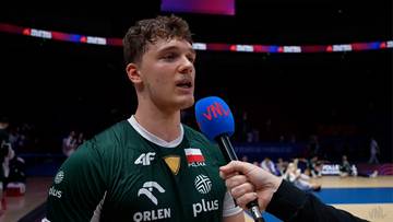 Mężczyzna w zielonej koszulce sportowej z godłem Polski udziela wywiadu do mikrofonu.