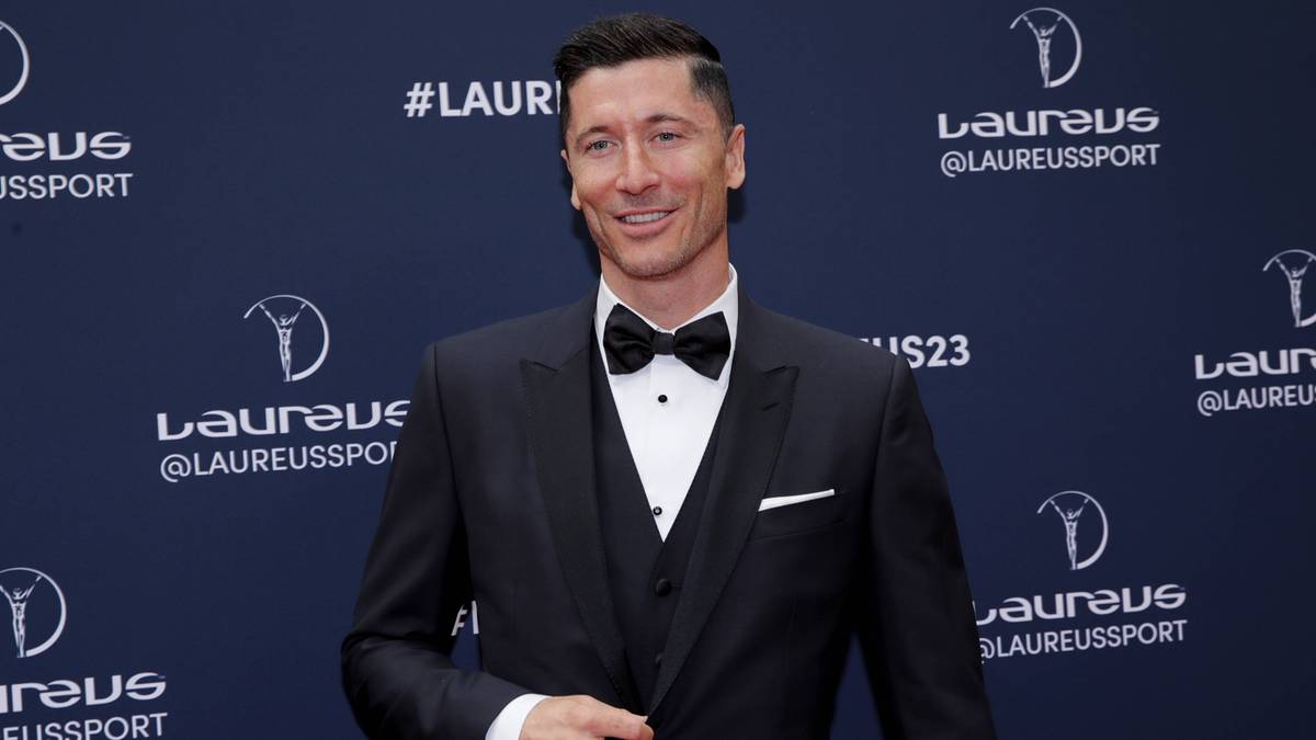 Robert Lewandowski w czarnym garniturze i muszce na tle granatowej ściany z logo Laureus.