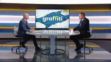 Janusz Cieszyński i inny mężczyzna siedzą przy stole w studiu telewizyjnym. Na ekranie za nimi widnieje napis "graffiti".
