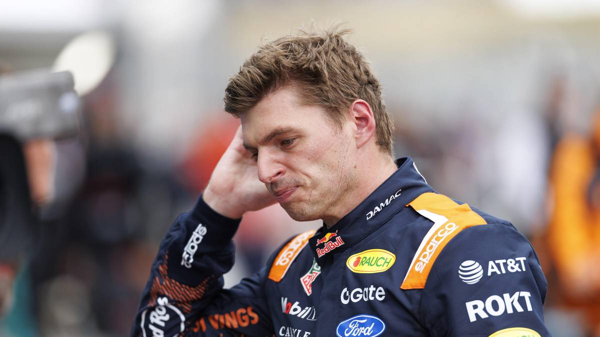 Max Verstappen, kierowca Formuły 1, w kombinezonie wyścigowym z logo zespołu Red Bull, trzyma rękę przy skroni, wyglądając na zmartwionego lub zmęczonego.
