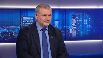 Mężczyzna w garniturze i krawacie siedzi na tle nocnego miasta.