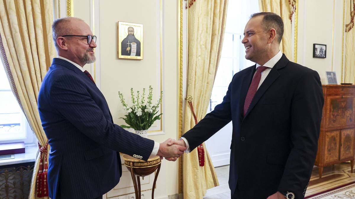 Dw&oacute;ch mężczyzn w garniturach ściska sobie dłonie wewnątrz eleganckiego pomieszczenia.