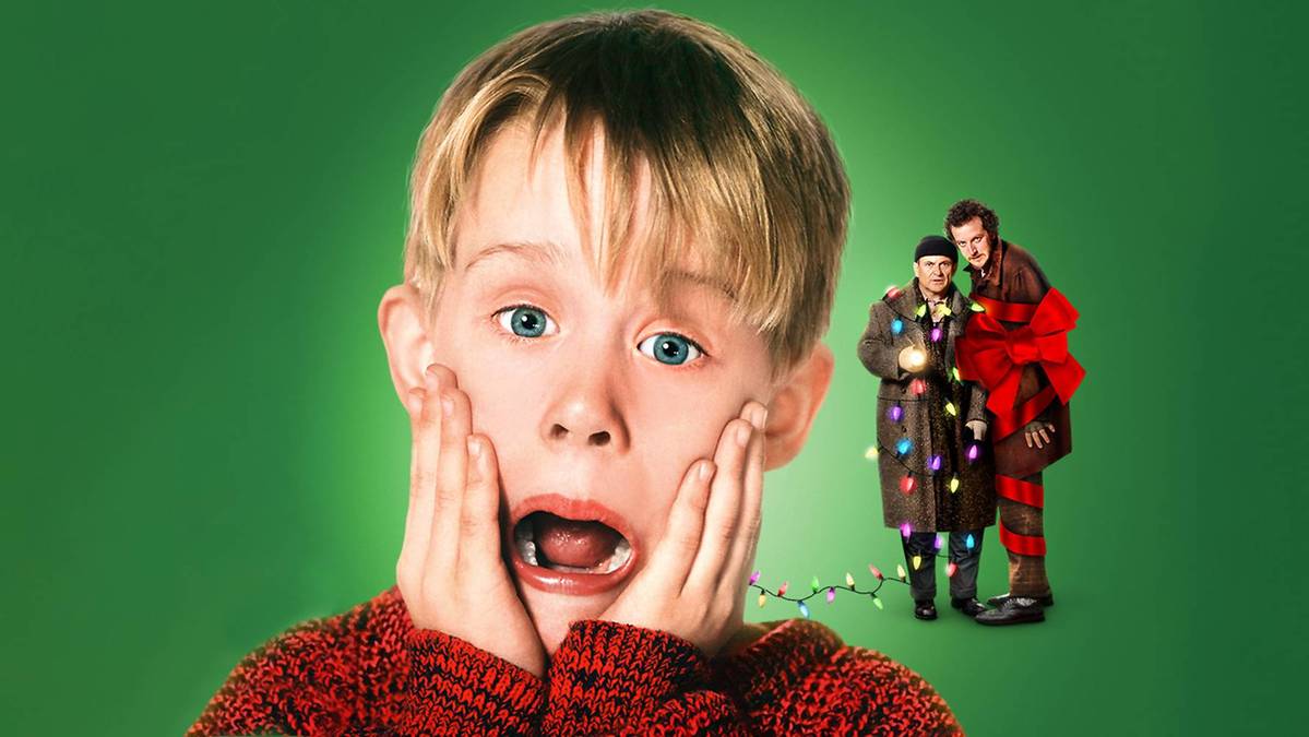 Zbliżenie na twarz Kevina McCallistera, z dłońmi przy policzkach i otwartymi ustami, na tle zielonym. W tle po prawej stronie widoczni są dwaj złodzieje owinięci w lampki choinkowe.