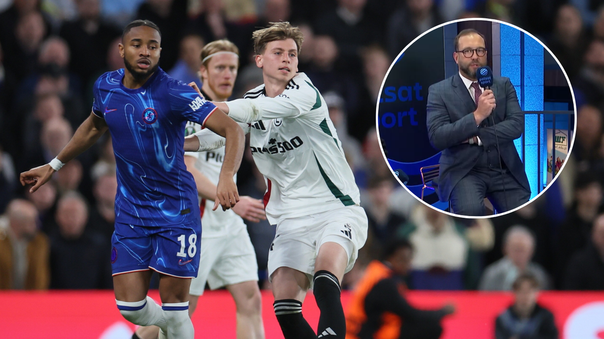 Piłkarze w białych i niebieskich strojach rywalizują na boisku podczas meczu piłki nożnej. W prawym górnym rogu widoczny jest mężczyzna w garniturze przemawiający przed kamerą.