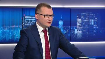 Paweł Szefernaker w okularach, ubrany w granatowy garnitur i czerwoną krawat, siedzi w studiu telewizyjnym.