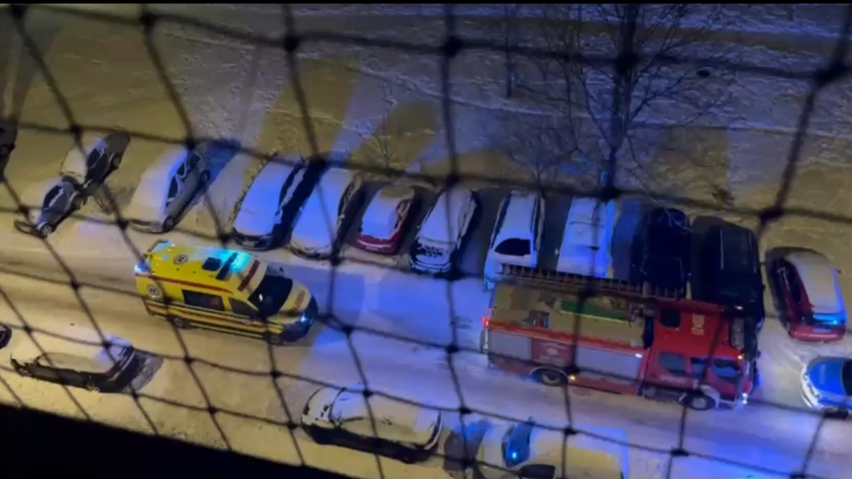 Samoch&oacute;d strażacki i karetka pogotowia stojące na zaśnieżonym parkingu obok zaparkowanych samochod&oacute;w.