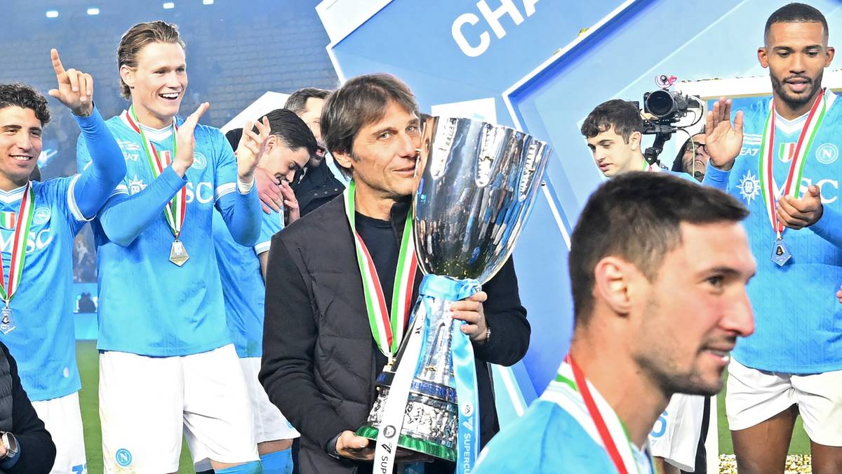 Trener Antonio Conte trzyma Puchar Superpucharu Włoch, otoczony przez radośnie świętujących zawodnik&oacute;w Napoli.