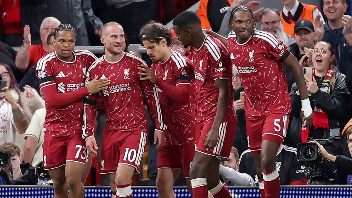 Piłkarze Liverpoolu w czerwonych strojach podczas meczu, patrzący w tym samym kierunku na tle kibic&oacute;w.