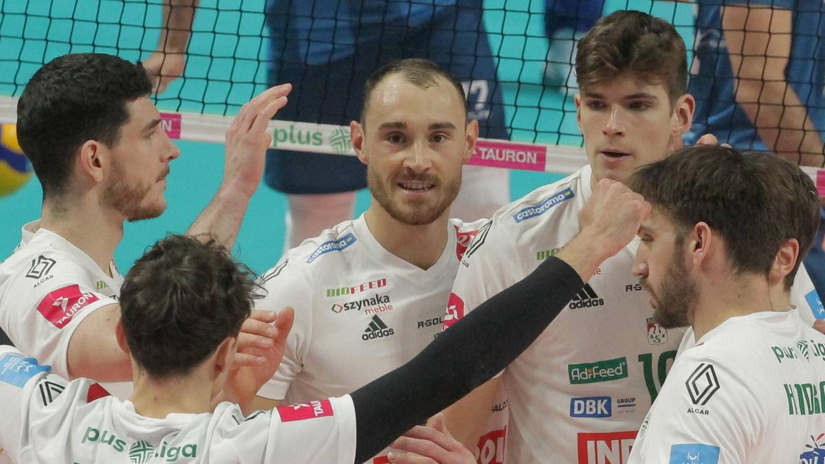 Siatkarze w białych koszulkach świętują na boisku, obejmując się i unosząc ręce w geście radości.