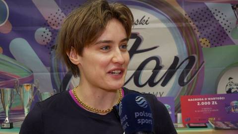 Katarzyna Zillmann, młoda kobieta o kr&oacute;tkich brązowych włosach, ubrana w ciemną bluzę z kolorowym kołnierzem i złotym łańcuszkiem, m&oacute;wi do mikrofonu z logo "Polsat Sport". W tle widoczne są puchary, baner z napisem "Stan" oraz tablice informacyjne.