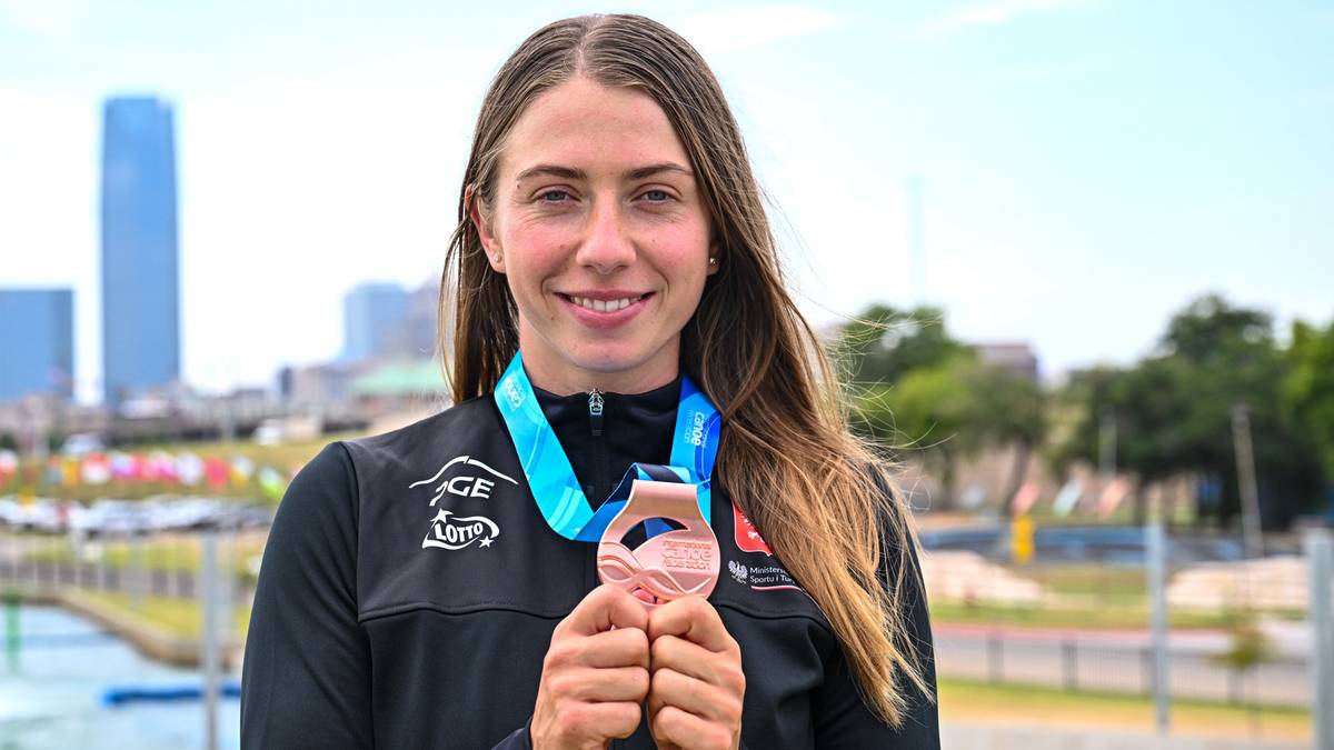 Uśmiechnięta kobieta w stroju sportowym trzyma medal na szyi, prezentując go przed obiektywem.