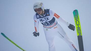 Skoczek narciarski w powietrzu, przygotowujący się do lądowania.