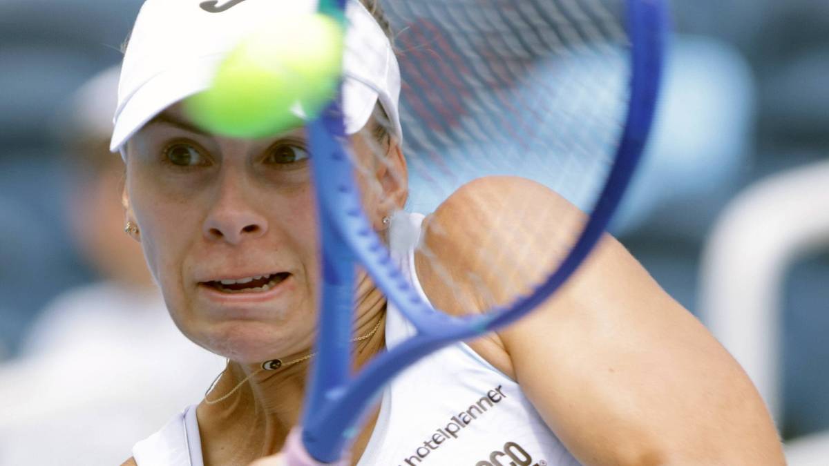 Tenisistka Magda Linette podczas meczu, w białej czapce i stroju sportowym, uderza piłkę rakietą.