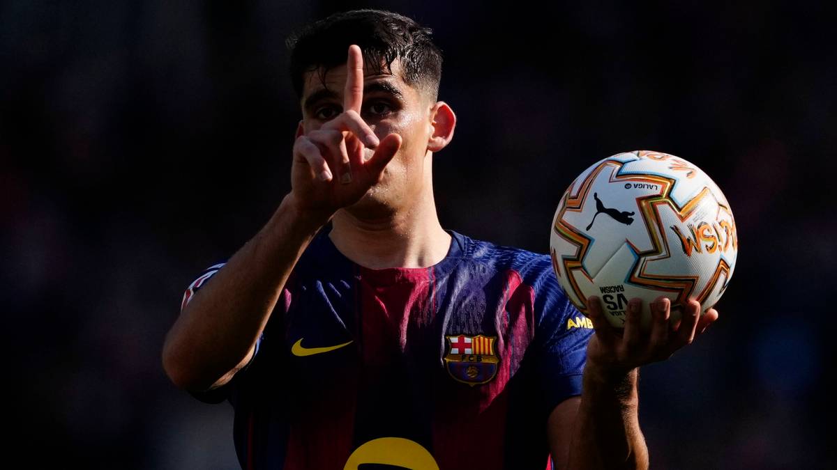 Piłkarz FC Barcelony trzymający piłkę i wykonujący gest palcami.