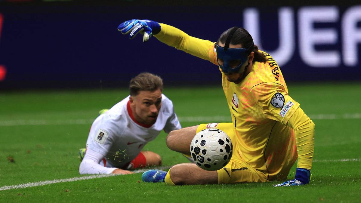 Dwóch piłkarzy na boisku, jeden klęczy z piłką, drugi obserwuje.