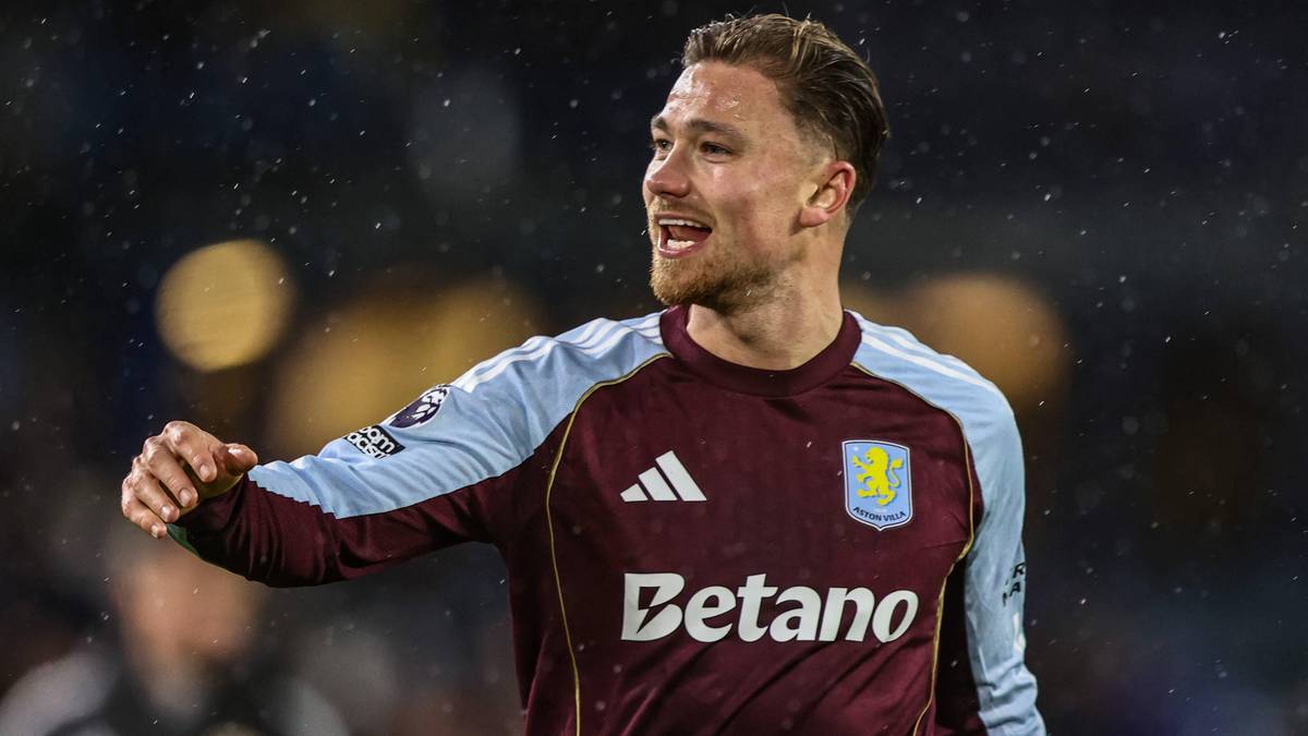 Piłkarz Aston Villi, Matty Cash, w bordowej koszulce z jasnoniebieskimi rękawami, uśmiecha się podczas meczu.